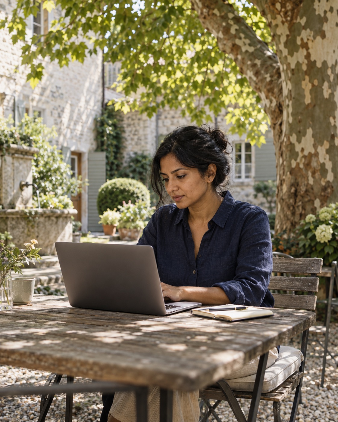 A business owner working on her laptop in a garden courtyard.